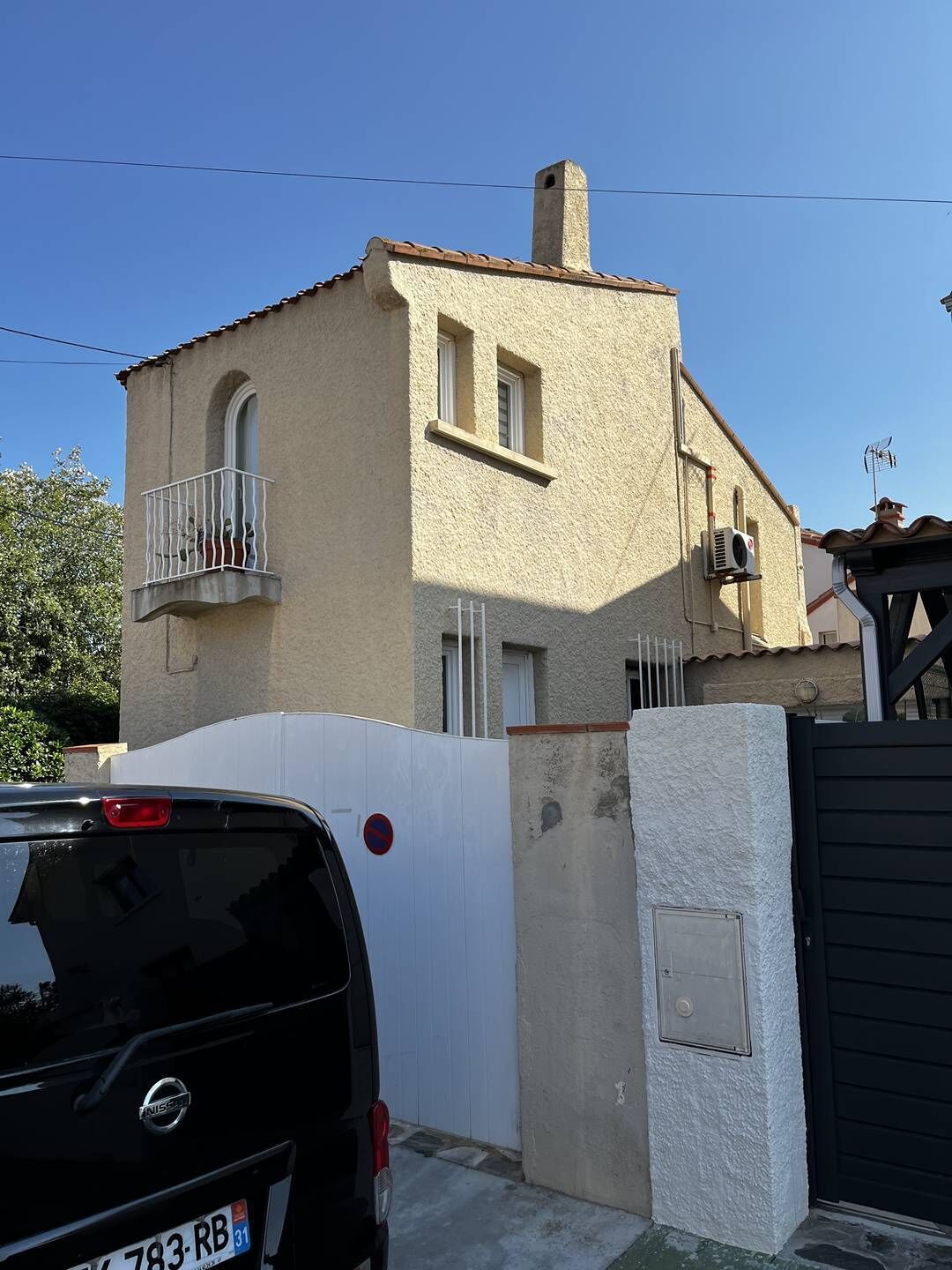 A two-story building with a balcony, a gate, and a parked car.