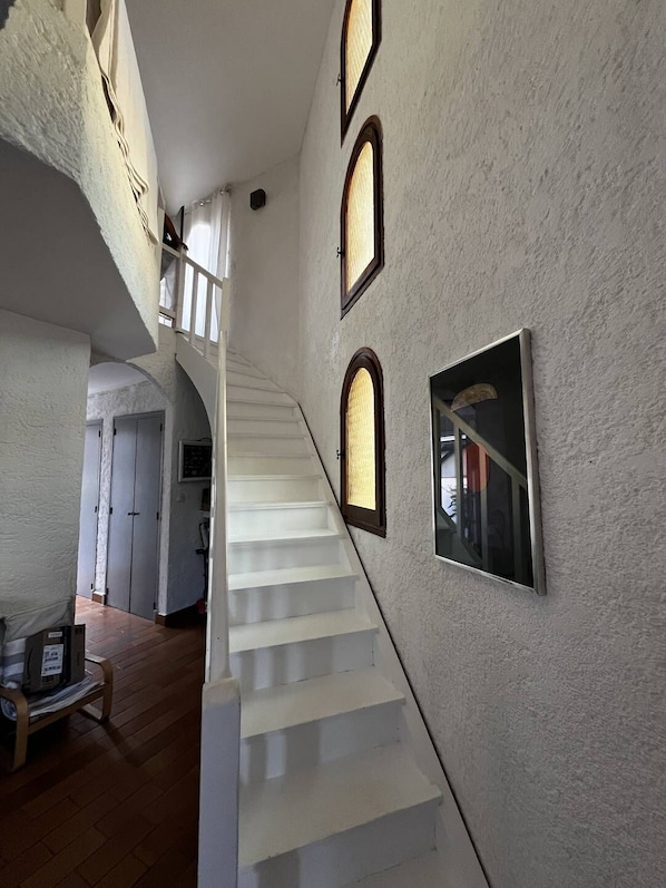 A staircase with white steps leading to a second floor, flanked by white walls and three arched windows.