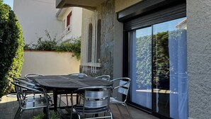 An outdoor patio with a round table and metal chairs, a stone wall, and a sliding glass door leading to a covered area. - Villa T4 type canétoise air-conditioned and near beach - 6ILEF56 (CANET PLAGE)
