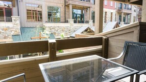 En balkon med et glasbord og en træbænk, der udover en gårdsplads med stenvægge og en lille pool.