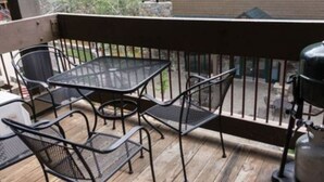 Une terrasse en bois avec une table et des chaises en métal, un barbecue et un distributeur d’eau.
