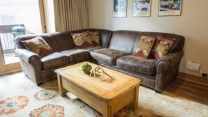 Un salon avec un canapé d’angle en cuir marron, une table basse en bois et un tapis à motifs.