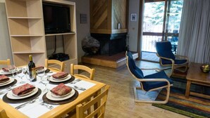 Ein Essbereich mit Tisch für vier Personen, einem Fernseher, einem Kamin und Blick ins Freie.