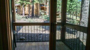 Eine Holzterrasse mit Metallgeländer, die zu einem überdachten Außenbereich mit Holzbauten und Bäumen führt.