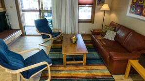 Ein Wohnzimmer mit einem braunen Ledersofa, zwei blauen Sesseln, einem Holztisch und einem farbenfrohen Streifen Teppich.
