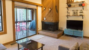 A living room with a fireplace, a television on a blue stand, and a sliding glass door leading to an outdoor area.