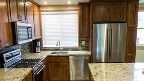 A modern kitchen with wooden cabinets, stainless steel appliances, granite countertops, and a window with blinds. - 4BR Spacious Condo | Private Deck & Fireplace (Truckee)