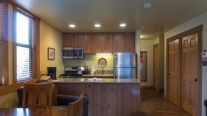 A compact kitchen with wooden cabinets, stainless steel appliances, and a dining area with a table and chairs. - Cozy Studio Condo with Fully Equipped Kitchen (Truckee)