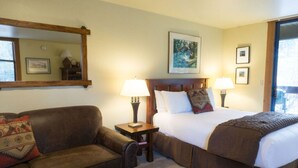 A hotel room with a bed, a sofa, a nightstand, a lamp, and a painting on the wall. - Cozy Studio Condo with Fully Equipped Kitchen (Truckee)