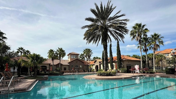 A swimming pool with clear blue water, surrounded by palm trees and lounge chairs.