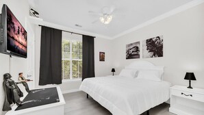 A bedroom with a bed, a nightstand, a TV, and a ceiling fan.