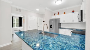 A modern kitchen with white cabinets, a blue marble countertop, and a stainless steel refrigerator.