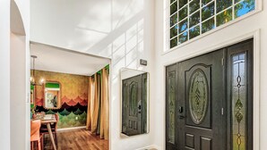 Un corridoio con zona pranzo, una porta nera con pannelli di vetro decorativi e un murale al muro.