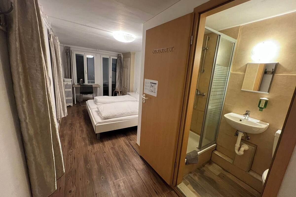 A hotel room with a bed, a desk, a shower, and a bathroom.