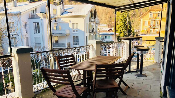 A wooden table and chairs on a balcony with a metal railing, overlooking a residential area with buildings. - Interlaken Linda Inn Lodge (Interlaken)