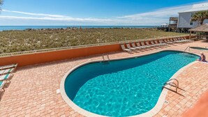 Ein gewundener Swimmingpool mit klarem, blauem Wasser, umgeben von einer Ziegelterrasse und Liegestühlen.