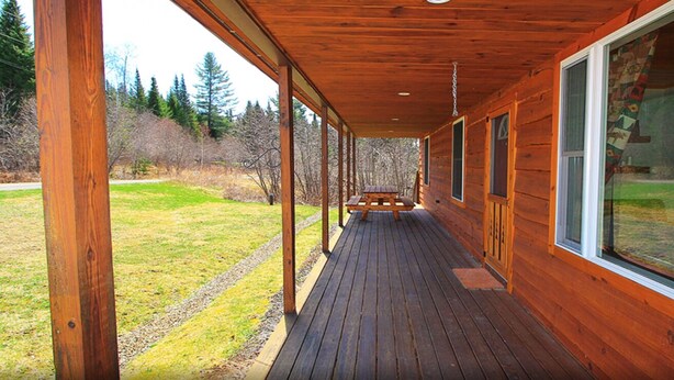 A wooden deck with a bench, large windows, and a view of a grassy area. - Rangeley Getaway (Rangeley)
