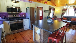 A kitchen with a central island, stainless steel appliances, and wooden flooring. - Rangeley Getaway (Rangeley)