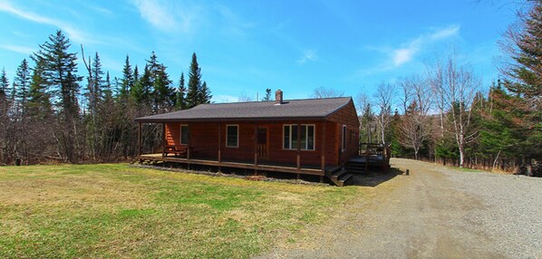 A single-story wooden cabin with a porch, surrounded by a gravel driveway and a forested area. - Rangeley Getaway (Rangeley)