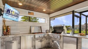 A modern kitchen with a built-in grill, a flat-screen TV, and a view of the outdoors.
