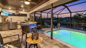 A modern kitchen with a large island, bar area, and a poolside seating area with a view of the pool and surrounding landscape.