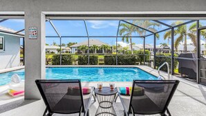 Ein Poolbereich mit zwei Liegestühlen, einem Tisch mit Getränken und Blick auf ein Wohngebiet.