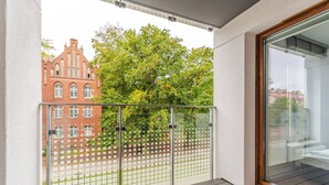 A balcony with a wooden floor, a glass door, and a view of a red brick building and trees.