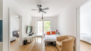 A modern bedroom with a bed, a desk, a TV, and a ceiling fan.