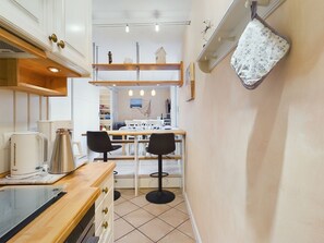 A compact kitchen with a wooden countertop, two bar stools, and a hanging pot rack.