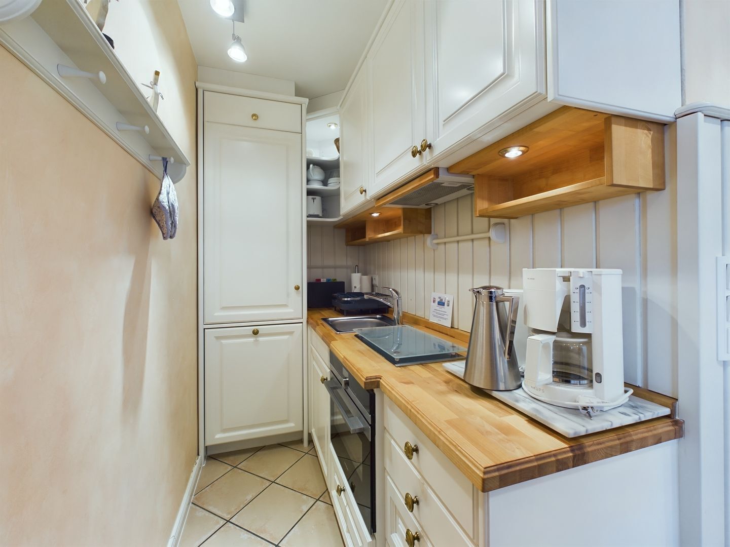 Una cucina compatta con pensili bianchi, un piano di lavoro in legno e una macchina per il caffè.
