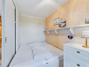 A bedroom with a bed, a dresser, a shelf with decorative items, and a wall with a painting.