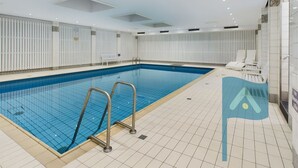 Una piscina con pareti e pavimento piastrellati, dotata di scalette metalliche e lettini da relax.