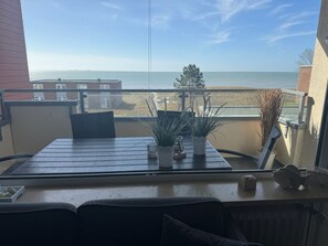 A balcony with a table, chairs, and potted plants overlooking a beach.