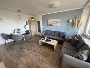 Een moderne woonkamer met een grijze bank, een salontafel, en een eethoek met stoelen en een tafel.
