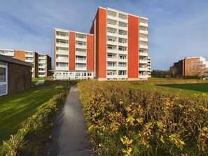 Un moderno edificio de apartamentos con varios pisos y balcones, rodeado de un césped bien cuidado y un camino.