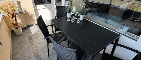 Un balcon avec une table et des chaises, des plantes en pot et une vue sur la plage.