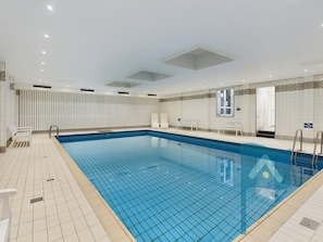 Une grande piscine intérieure à l’eau d’un bleu limpide, avec des murs carrelés et un plafond doté d’un éclairage encastré.