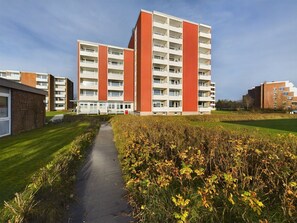 Moderni kerrostalo, jossa on useita kerroksia ja parvekkeita, ja sen ympärillä on hyvin hoidettu nurmikko ja kävelyreitti.