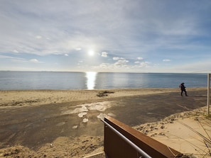 Une plage où une personne se promène, un ciel dégagé et le soleil qui se reflète sur l’eau.