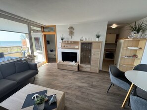 Een moderne woonkamer met een bank, salontafel en een open haard. Er is een eethoek met een tafel en stoelen. De kamer heeft houten vloeren en uitzicht op het landschap.