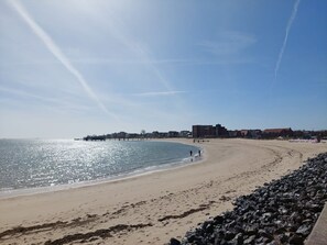 Une plage avec un ciel dégagé, une jetée et des bâtiments en arrière-plan.