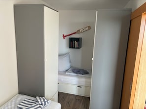 A bedroom with a bed, a nightstand, a shelf with books, and a door.