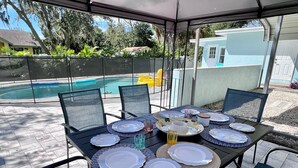 An outdoor patio with a table set for four, overlooking a swimming pool and a backyard with a house and greenery. - Pool house 3 bed 2 bath, 1 mile from the beach (Largo)