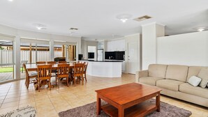 A modern kitchen with white cabinets, a central island, and a dining area with wooden chairs and a table. - D3 Ski Ranch. 5-bedroom waterfront home and private jetty. (Bundalong)