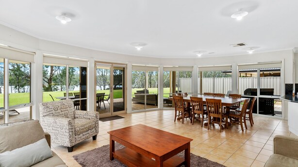 A spacious living area with a dining table and chairs, a sofa, and a coffee table. - D3 Ski Ranch. 5-bedroom waterfront home and private jetty. (Bundalong)