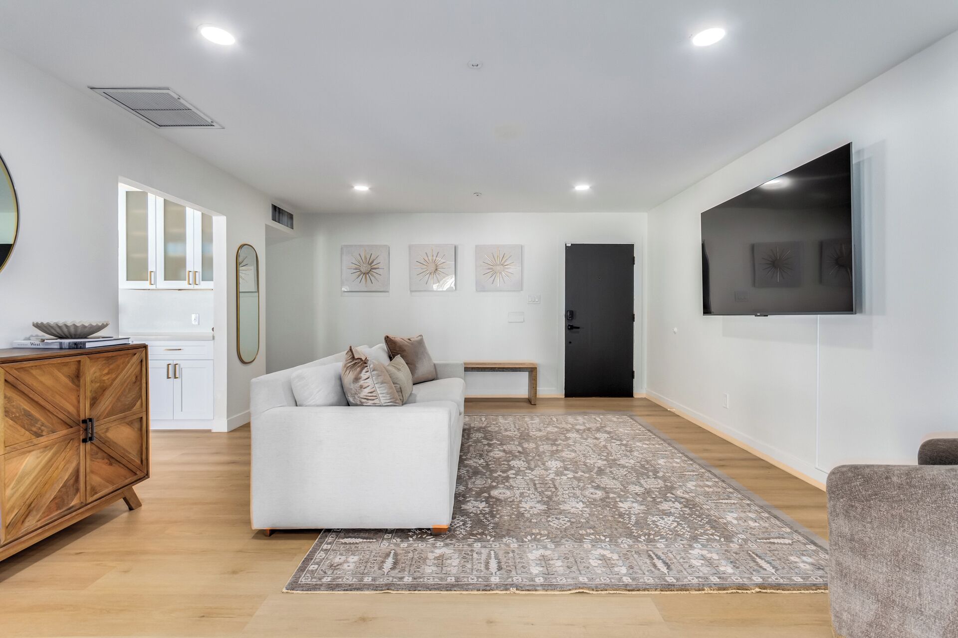 A modern living room with a white sofa, a wooden cabinet, a flat-screen TV, and a patterned rug.