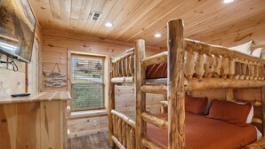 L’intérieur d’un chalet en bois, avec un lit superposé, une fenêtre donnant sur un paysage agréable et un bureau en bois.