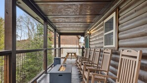 Une véranda couverte avec des chaises en bois et un foyer.
