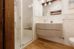 Een badkamer met een glazen douchecabine, een houten vloer, een wit wastafelmeubel met spiegel erboven en een wit toilet.