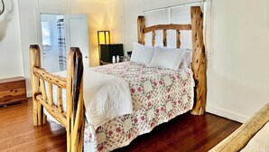 A room with a wooden bed frame, a white wall, and a wooden floor.